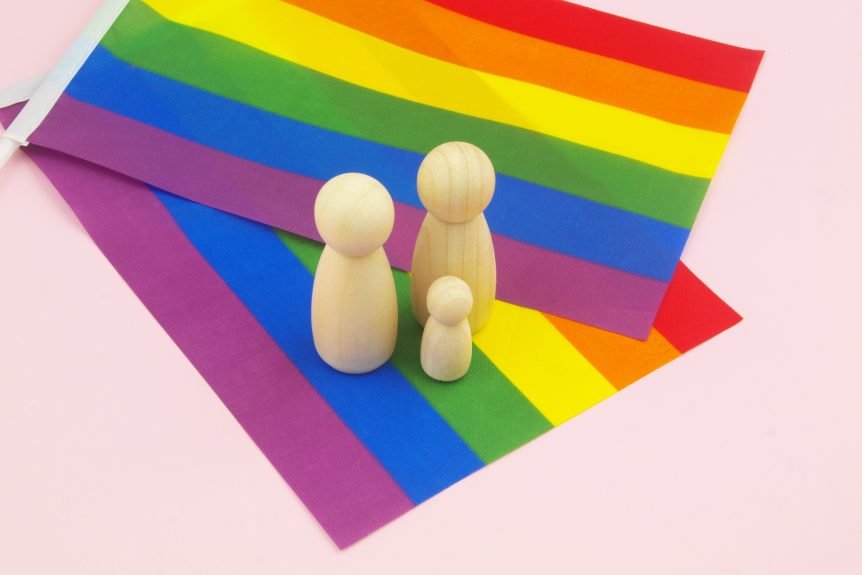 Two female wooden figures and one kid figure on the LGBT flag